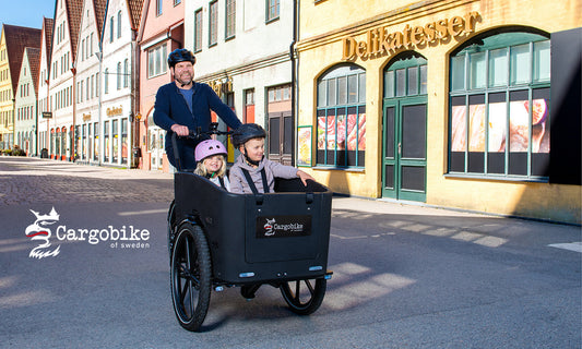 Vater, der seine beiden Kinder mit einem Lastenrad von Cargobike of Sweden transportiert.